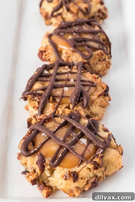 Golden Caramel Thumbprint Bites 3 A stack of golden brown Caramel Thumbprint Cookies with melted caramel in the center and a chocolate drizzle on top.