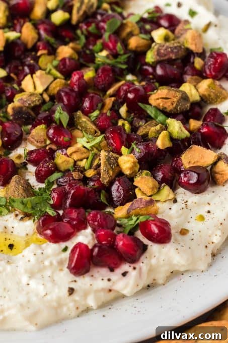 Close-up shot of creamy whipped feta dip garnished with pistachios and pomegranate seeds on a white plate.