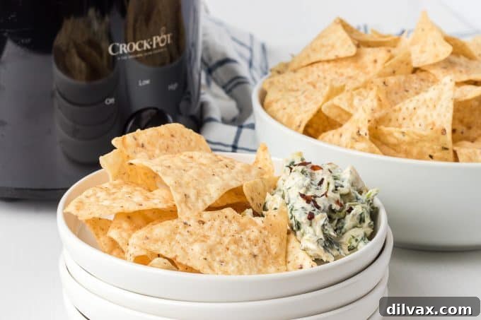 Warm & Cheesy Slow Cooker Spinach Artichoke Dip 2 Creamy Crockpot Spinach Artichoke Dip ready to serve in a slow cooker, surrounded by various dippers like crackers and vegetables.