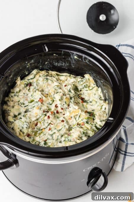 Warm & Cheesy Slow Cooker Spinach Artichoke Dip 7 A slow cooker filled with bubbling, creamy artichoke dip with spinach, ready to be served at a party.