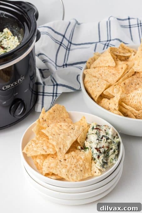 Warm & Cheesy Slow Cooker Spinach Artichoke Dip 8 A close-up of a serving of Crockpot Spinach Artichoke Dip, garnished with a sprig of fresh parsley, emphasizing its creamy texture and readiness to eat.