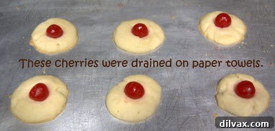 Drizzling melted chocolate over maraschino cherries in cookies