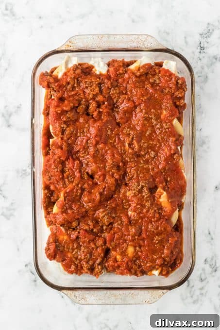 A baking dish full of stuffed pasta shells ready for the oven, topped with sauce