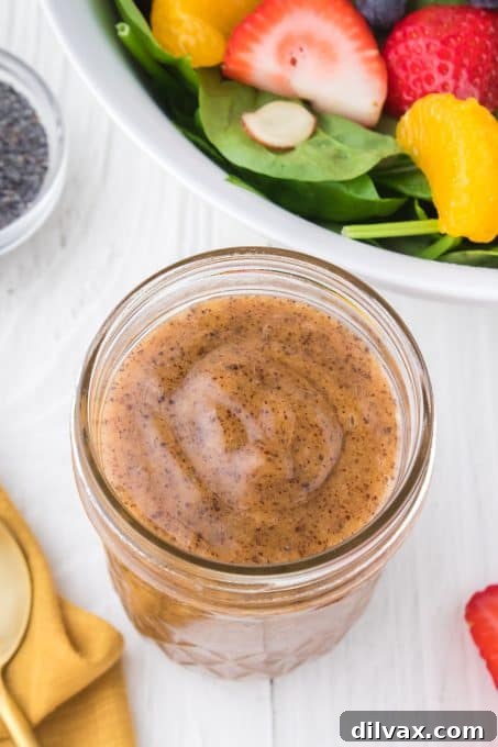 A glass mason jar of vibrant poppy seed dressing sitting on a rustic wooden surface, ready for use.