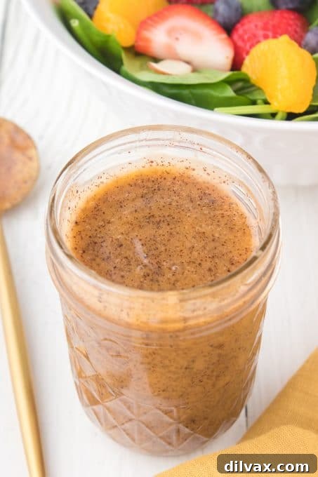 Creamy Poppy Seed Dressing 7 A rustic glass jar filled with golden poppy seed salad dressing on a wooden surface.