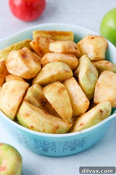 A large mixing bowl filled with sliced apples, generously coated with a mixture of sugar and cinnamon, ready for baking.
