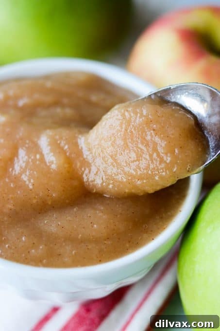 A spoonful of chunky baked applesauce being lifted from a white bowl, showing the steam and inviting texture.