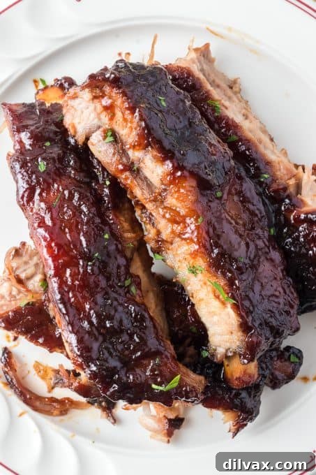 A chef's knife slicing through oven-baked St. Louis style pork ribs on a wooden cutting board.