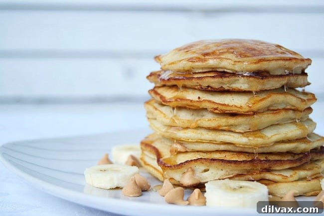 Fluffy pancakes with golden-brown edges, topped generously with sliced bananas, melted peanut butter chips, and a drizzle of maple syrup, promising an unbelievable breakfast experience.