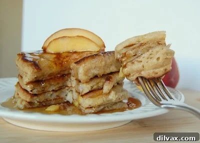 A stack of golden Cinnamon Peach Pancakes, with visible pieces of cooked peaches and a sprinkle of cinnamon, served on a white plate and garnished with fresh peach slices, inviting a delicious breakfast.