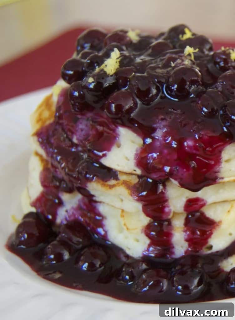 A beautifully arranged plate of Lemon Ricotta Pancakes topped with a vibrant blueberry compote and a dusting of powdered sugar. The pancakes are light and airy, promising a refreshing and elegant breakfast or brunch.
