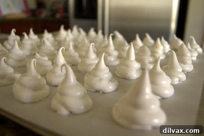 Piping meringue onto a baking sheet to form ghost shapes.