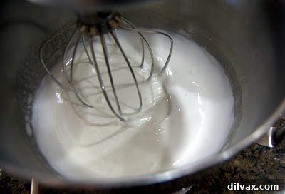 Egg whites being whipped in a stand mixer, starting to form soft peaks.