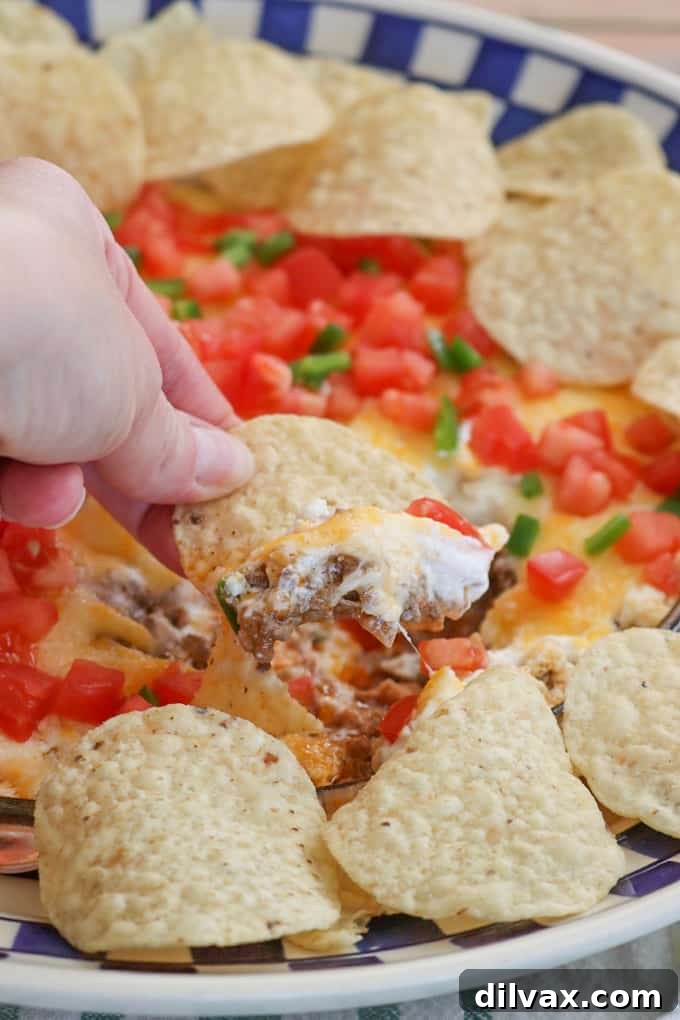 This Taco Dip is an incredibly easy and fun-to-serve game day dish, featuring four delicious layers of refried beans, taco-seasoned ground beef, sour cream, and Mexican cheese, topped with fresh diced tomato and jalapeño, served with tortilla chips. It's a guaranteed fan favorite!