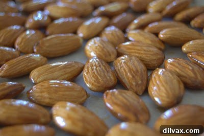 Almonds being tossed with olive oil in a bowl before baking.