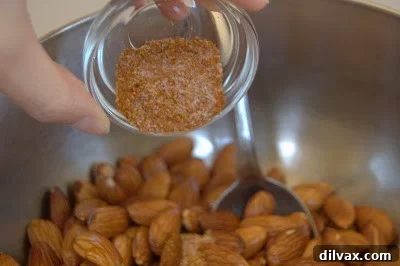 Warm roasted almonds being tossed with the spice mixture in a bowl.