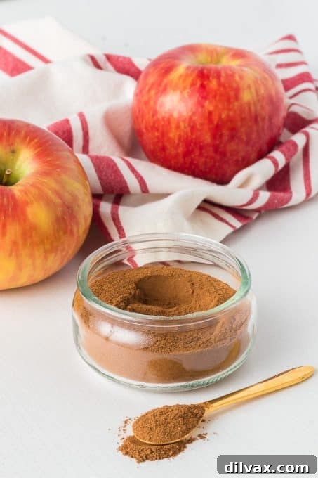 Autumn Spice Blend 11 Two glass jars filled with homemade Apple Pie Spice on a rustic wooden board, next to fresh apples.