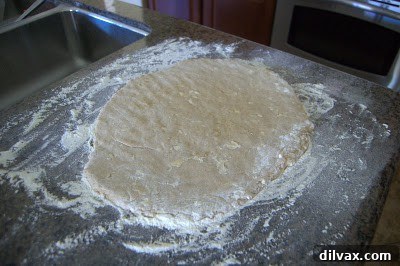 Doughnut dough being cut with a doughnut cutter on a floured surface.