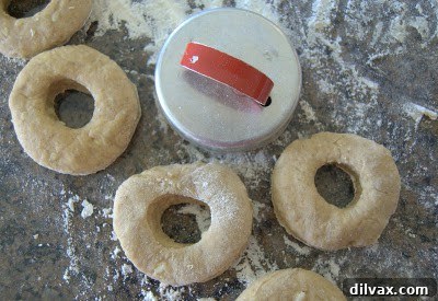 Several raw doughnut rings and holes arranged on a baking sheet, ready for baking.