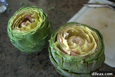 Hands gently opening an artichoke's leaves to prepare for seasoning.