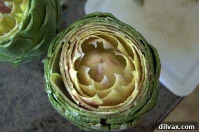 A lemon half being rubbed over the opened leaves of an artichoke.