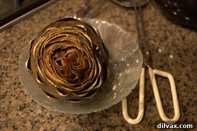 A perfectly baked artichoke, unwrapped and served on a plate with melted butter for dipping.