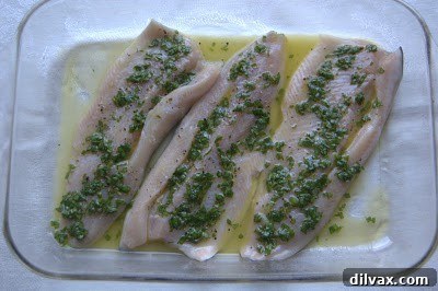 Basil and lemon mixture being evenly spread over trout fillets in a baking dish.