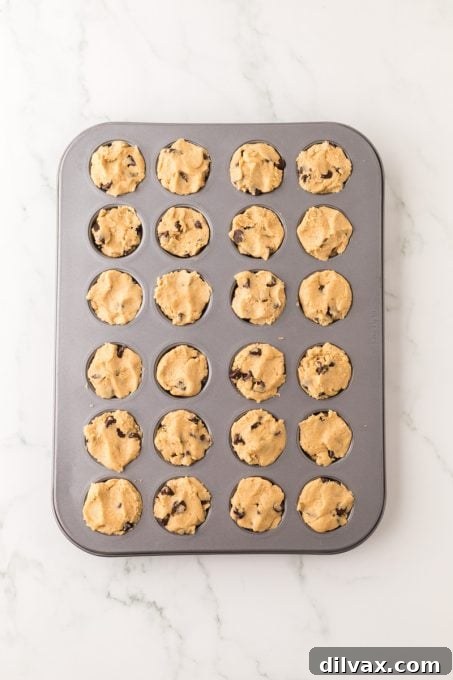A mini muffin tin filled with unbaked peanut butter cookie dough, ready for the oven, hinting at the deliciousness to come.