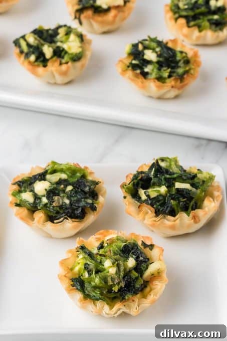 Phyllo dough shells filled with a vibrant green spinach and Feta filling, ready for baking.