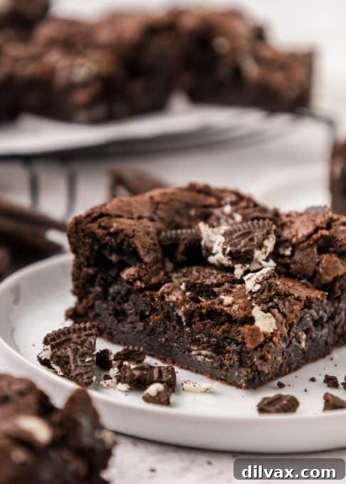 A close-up of a plate of warm Oreo Brownies, topped with a scoop of melting vanilla ice cream and chocolate sauce.