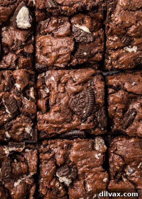 Several fudgy Oreo Brownies stacked neatly on a white plate, showcasing their thick texture and cookie bits.