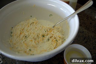 Shredded potatoes mixed with cream, cheese, and green onions in a bowl