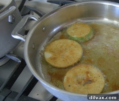 Zucchini slices sizzling and browning in a hot skillet with olive oil.