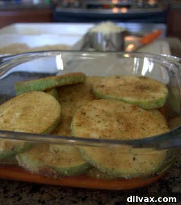 The first layer of sautéed zucchini being arranged in a baking dish with sauce.