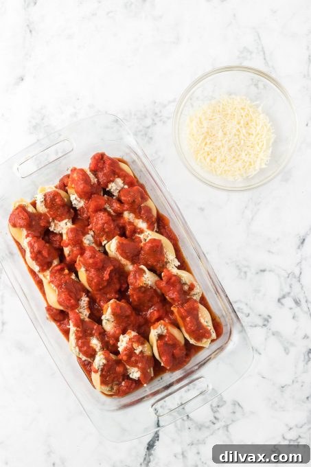 Pasta sauce being poured over stuffed shells with chicken, ready for the oven.