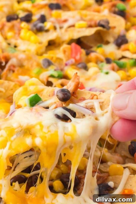 Pulling a single nacho off the tray, showcasing the cheese pull and generous toppings.