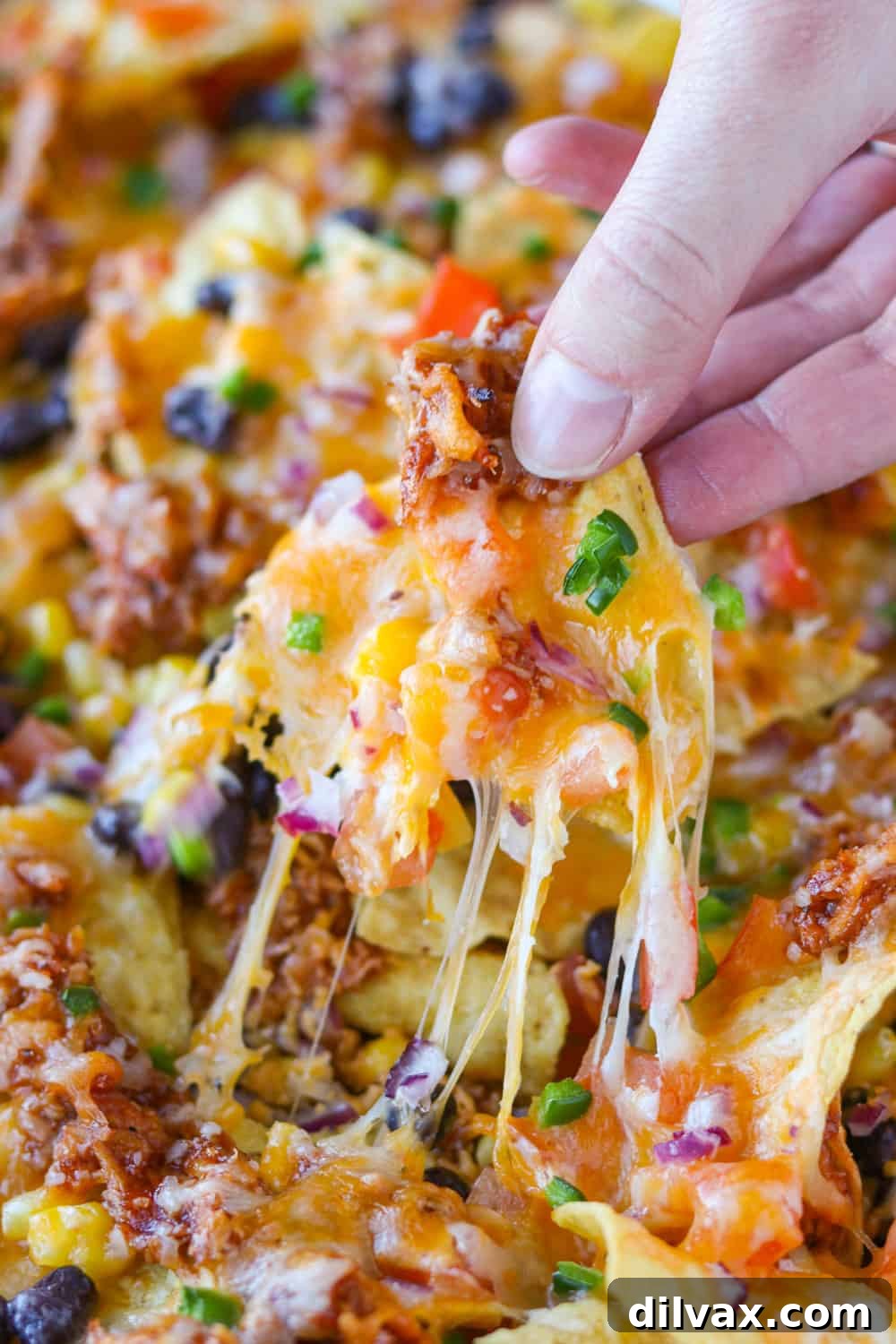 Close-up of a nacho with a perfect cheese pull, showcasing melted cheese and BBQ chicken