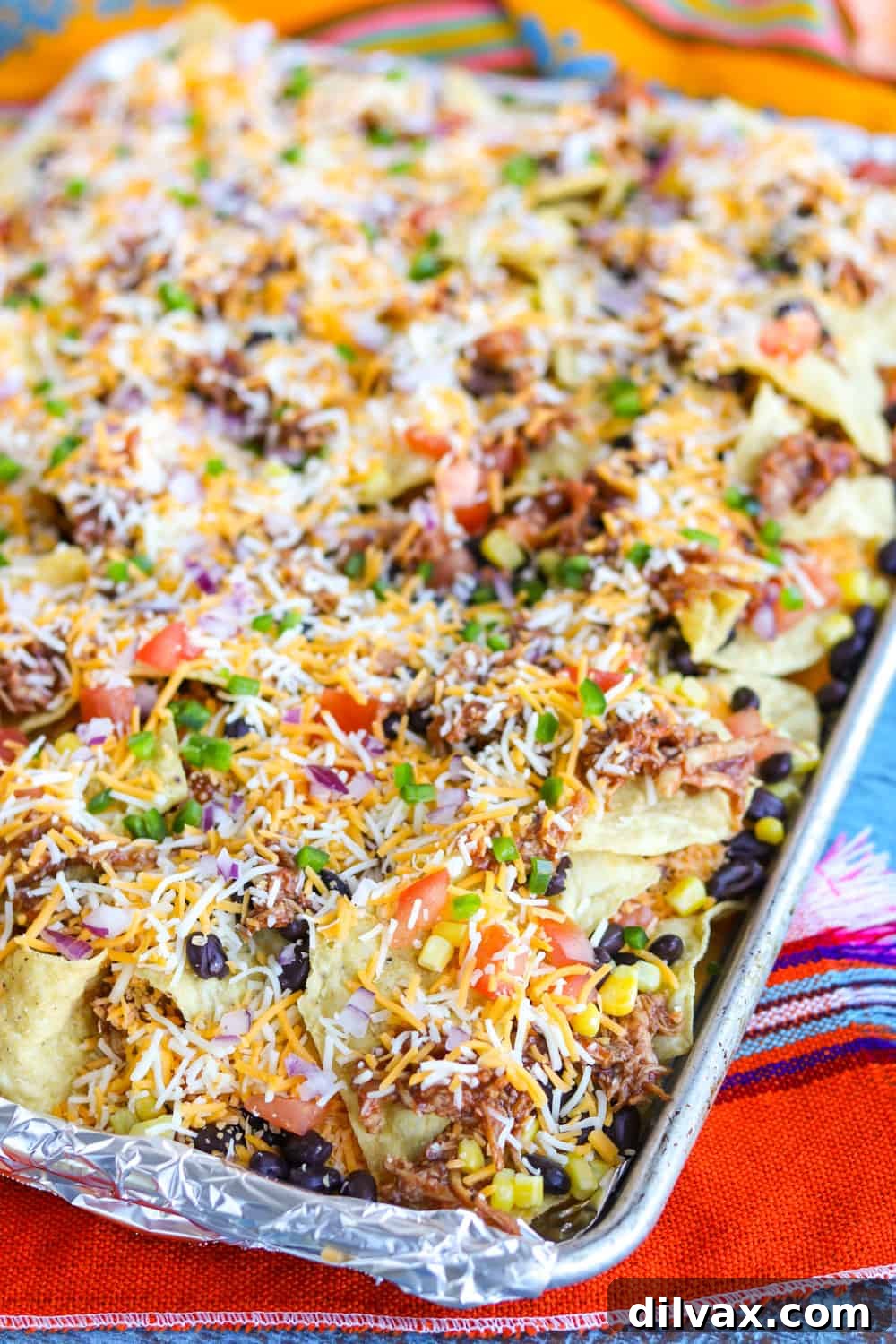 Sheet pan of Chicken Nachos ready to be baked, showing layered ingredients
