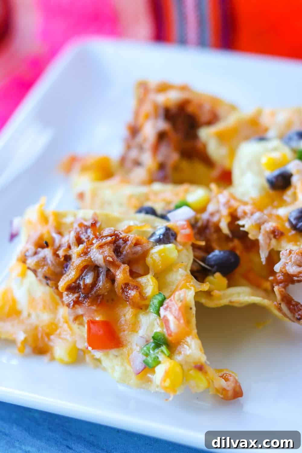 A plate of loaded nachos showcasing shredded BBQ chicken, corn, diced tomatoes, black beans, melted cheese, and jalapeño.