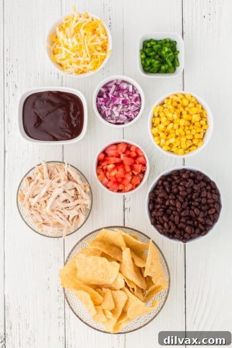 A collection of fresh ingredients laid out, including shredded chicken, tomatoes, corn, black beans, red onion, jalapeño, and cheese, ready for the BBQ chicken nachos.