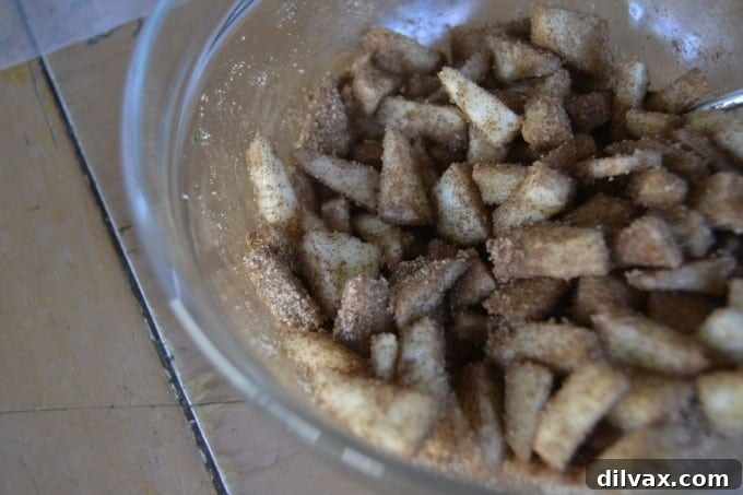 Diced fresh apples being tossed with cinnamon and sugar in a bowl