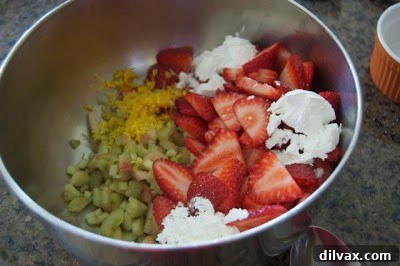 Freshly sliced strawberries and chopped rhubarb mixed with sugar, cornstarch, and lemon zest in a bowl for the galette filling.