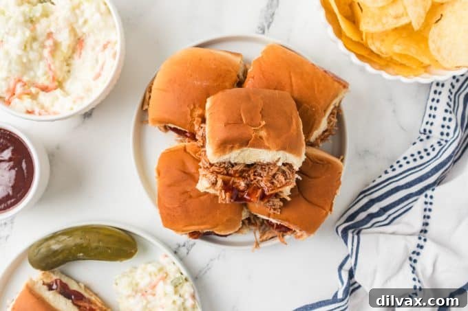 A platter of BBQ Chicken Sliders, garnished with fresh herbs and served with extra barbecue sauce for dipping.