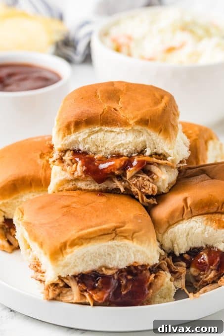 Perfectly assembled shredded chicken sandwiches with BBQ sauce on a cutting board, ready for serving.