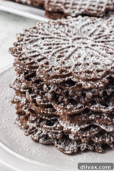 A stack of beautifully patterned chocolate pizzelles, dusted with powdered sugar, ready to be enjoyed.