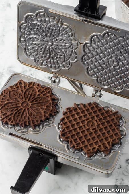 A pizzelle maker with several chocolate cookies freshly baked and ready to be removed.