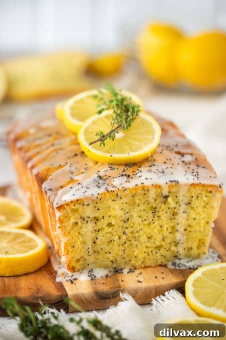 Bright Lemon Poppy Seed Loaf 7 A glazed quick bread on a wooden cutting board, garnished with fresh lemon slices.