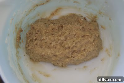 The flour has been stirred into the cookie batter, resulting in a cohesive mixture with visible nut pieces and an even consistency.