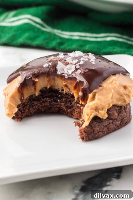 A Buckeye Cookie with a bite taken out, showing the perfect layers of brownie, peanut butter, and glossy chocolate ganache.