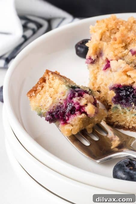 A fork taking a bite from a slice of Blueberry Crumb Cake, showing the moist interior.